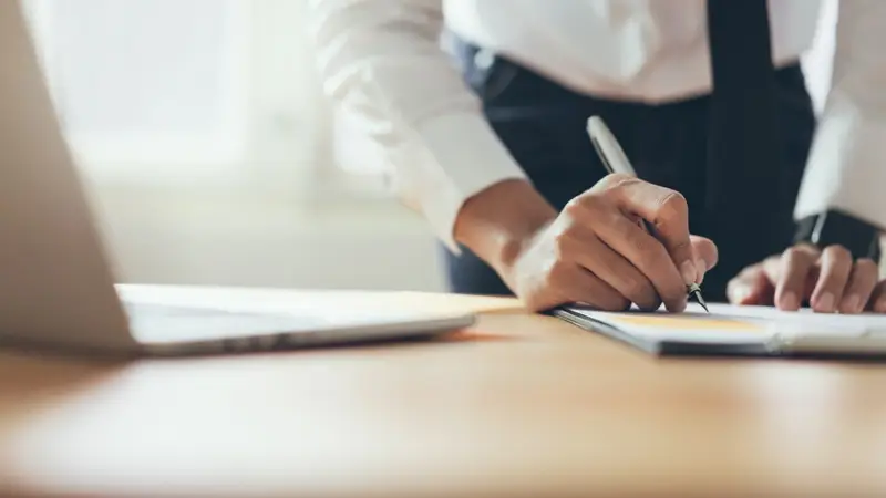 Businessman signing a document at a laptop Belinos Consulting London